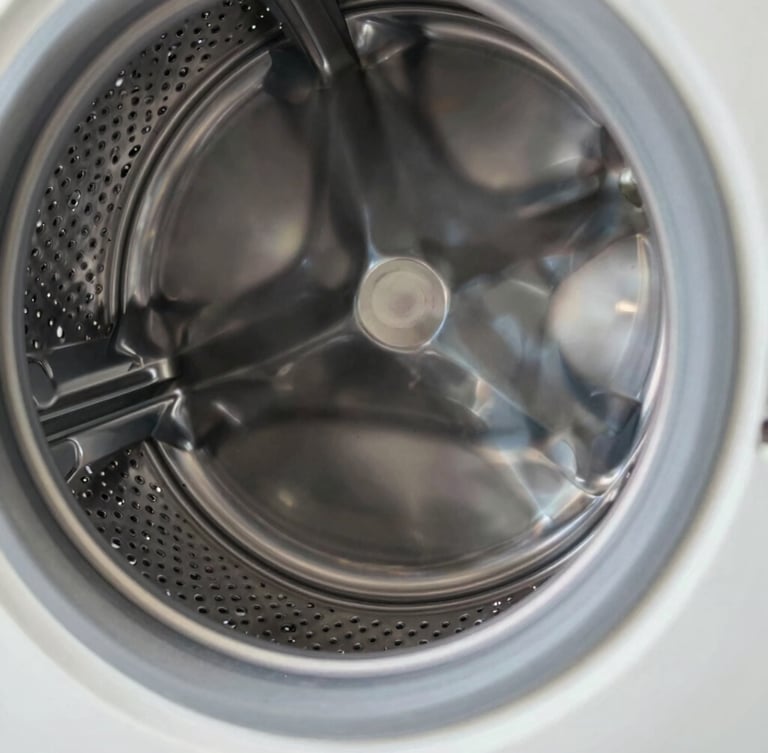 Macro close-up of a clean stainless steel washing machine drum, bright natural light reflecting off the metallic texture, sharp focus on the precision-milled drain holes, technical and clean.