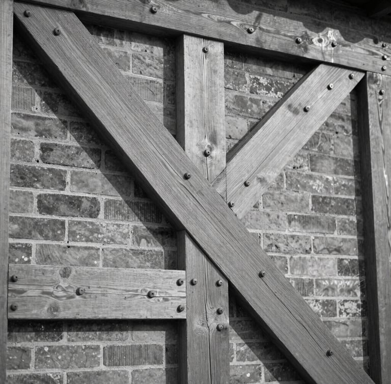Black and white architectural detail crop of heavy timber framing and original iron bolts in a brick wall, natural side lighting, high contrast.