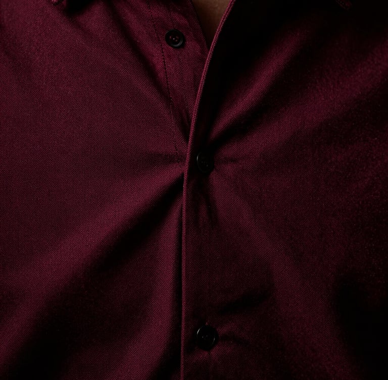 Macro close-up of heavy oxblood-red shirting seams and zero-tension weave texture, high-contrast directional studio lighting, deep shadows, medium format film