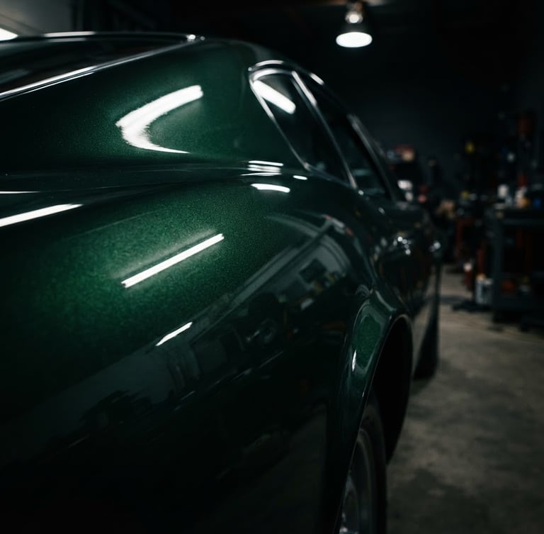 Macro detail of a flawless dark green metallic car paint finish reflecting dramatic workshop lighting, deep shadows, 50mm lens, rich metallic reflections.