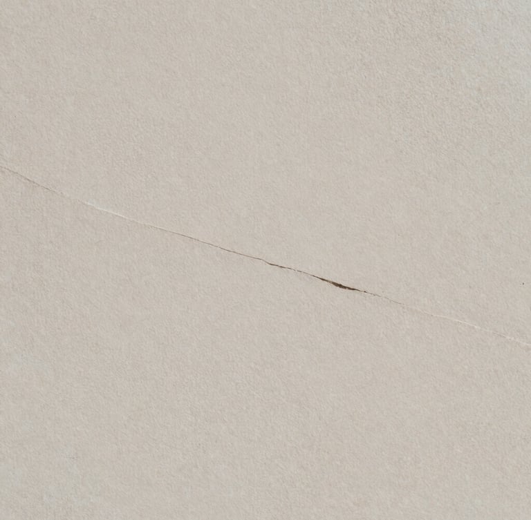 Minimalist editorial photography, soft diffused north-facing daylight. An extreme close-up of natural stone texture with a subtle, elegant crack running diagonally, casting quiet shadows. Matte paper texture, muted mineral tones, 35mm film.