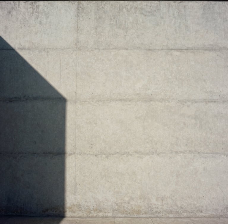 Wide-angle architectural elevation of raw concrete facade, sharp geometric shadows cast by natural daylight, minimalist composition, medium format film.