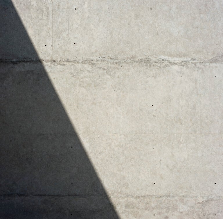 Extreme close-up of raw board-formed concrete wall, sharp diagonal shadow from natural daylight, minimalist editorial framing, medium format film texture
