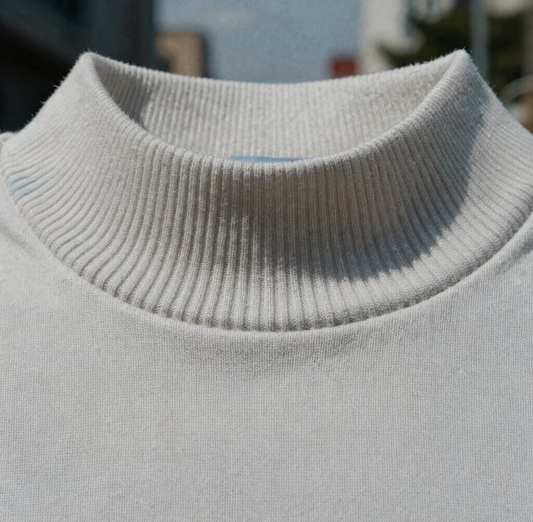 Macro close-up of heavy organic cotton fabric grain and thick ribbed collar, raw texture detail, cool overcast natural daylight.