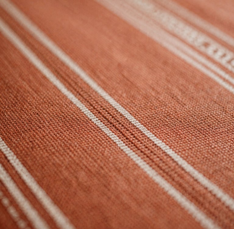 Macro close-up of warm terracotta hand-woven Indonesian tenun textile, rich organic thread textures, soft natural side-light, shallow depth of field, 35mm film