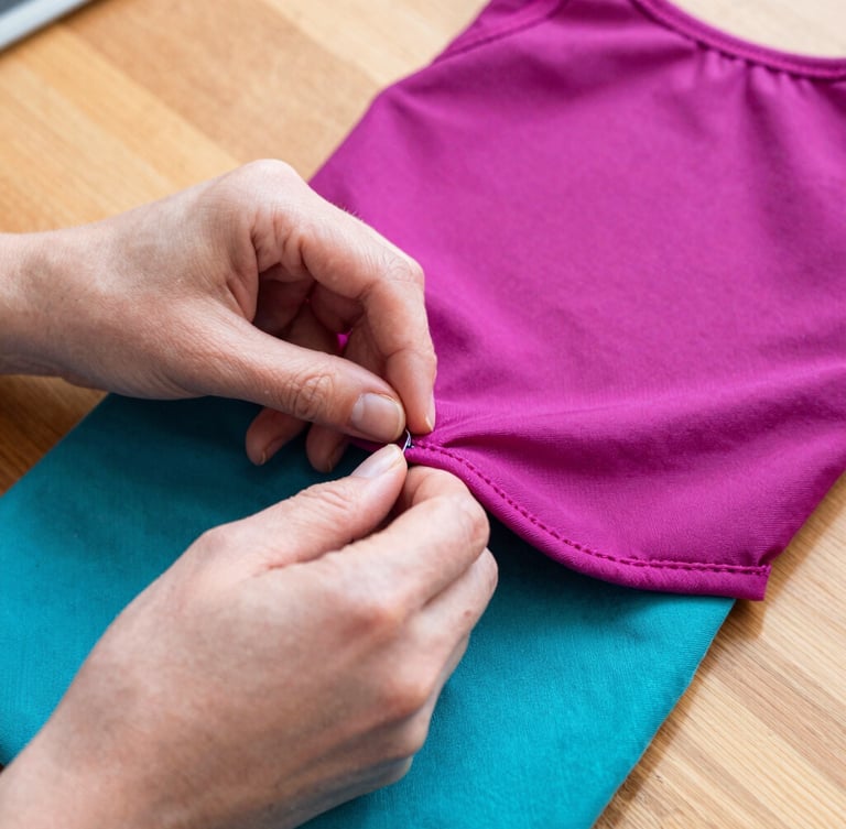 Close-up shot of hands carefully stitching a magenta pet garment on a wooden table, warm daylight, focusing on the neat hidden seams and fabric texture