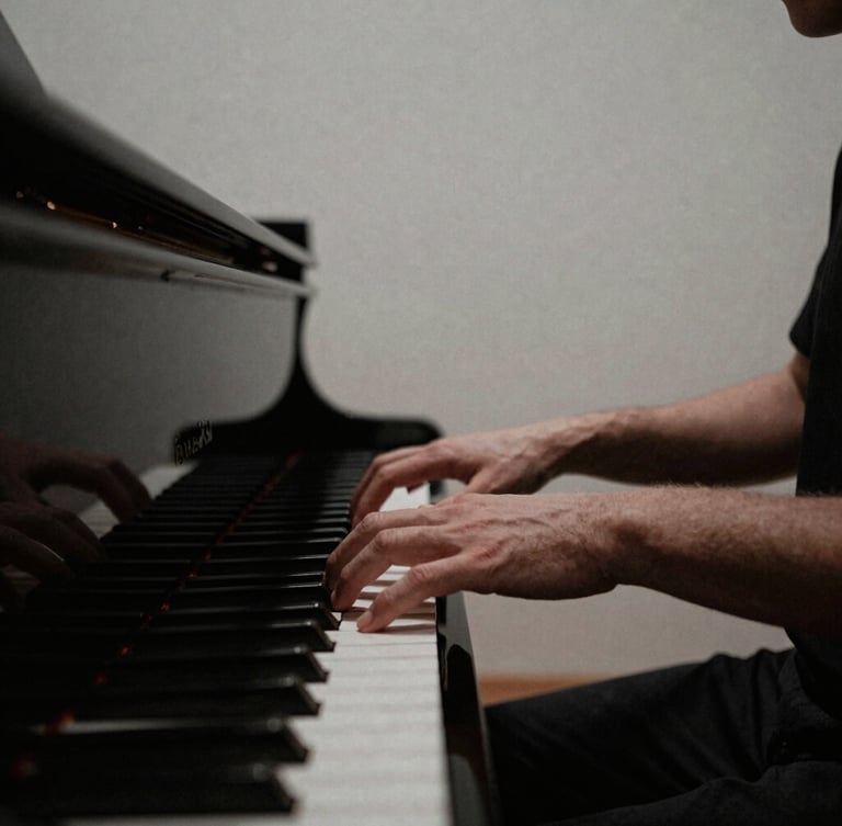 Hands of a musician gently playing a grand piano in a quiet, sunlit chapel, minimalist composition, deep muted tones, 35mm film grain