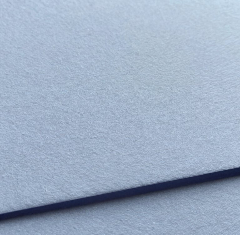 Close-up of premium textured cotton paper collateral with blind debossing, soft overcast daylight, muted blue and charcoal tones, macro shot