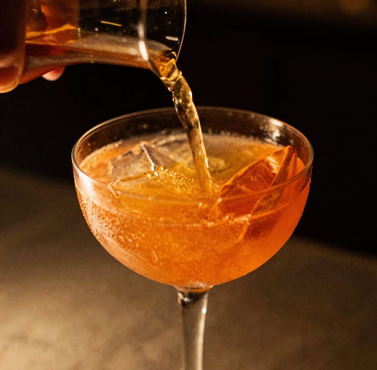 Close-up of a vibrant, garnished cocktail being poured, warm low-key evening light with rich golden accents, shallow depth of field, 35mm film.