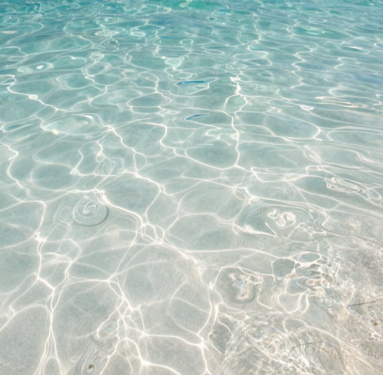 Extreme close-up of crystal-clear Maldivian water rippling over white sand under soft morning light, ocean-tinted tones.