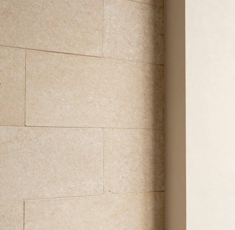 Detailed close-up of premium warm limestone block wall meeting smooth plaster, soft natural side lighting, minimalist architectural detail.