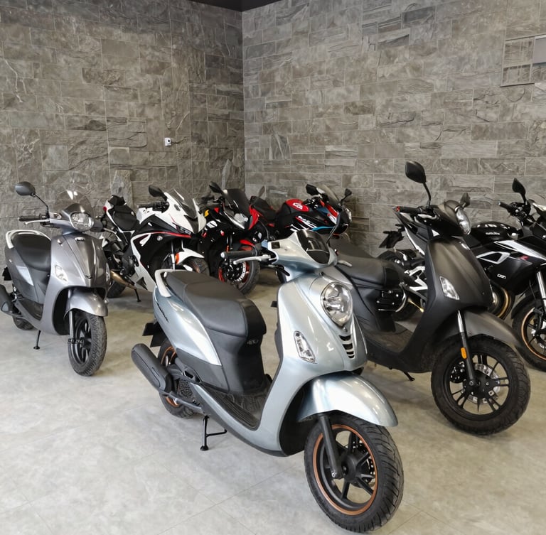 Wide shot of a clean motorcycle showroom interior, organized sections of automatic scooters and sportbikes, modern garage design with slate-grey walls, bright natural light