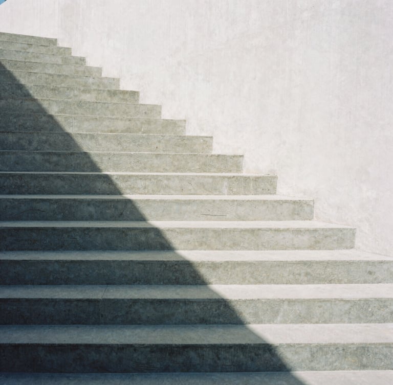 Minimalist architectural photography of a concrete staircase casting sharp geometric shadows under soft daylight, high contrast slate and white tones, 35mm