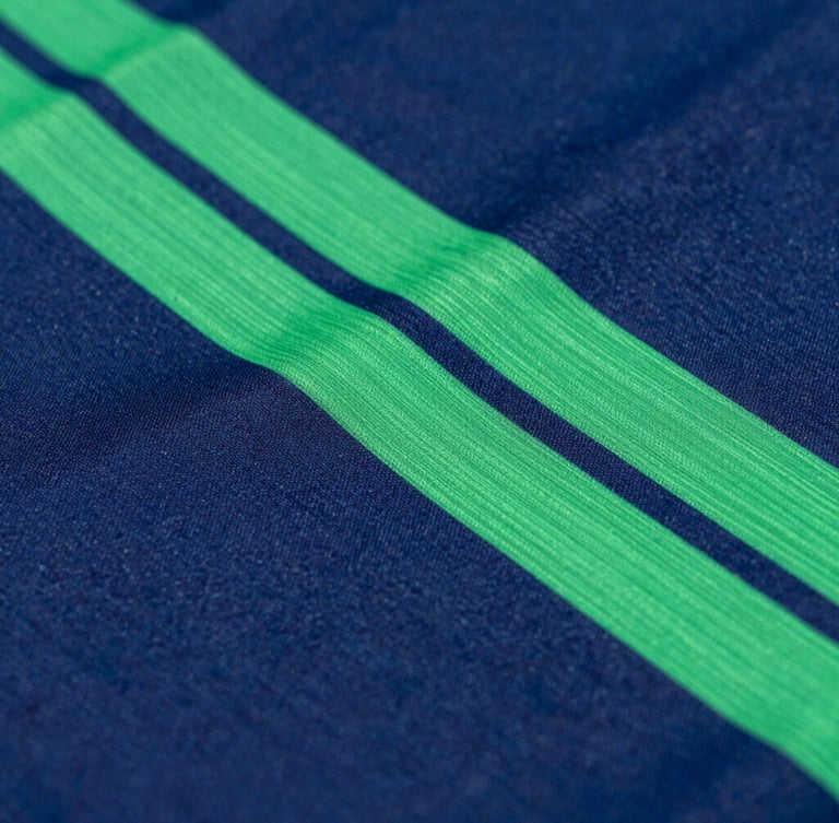 Detail macro shot of high-performance athletic fabric, vibrant sublimated green and blue geometric patterns, crisp studio lighting, deep navy background, sharp focus, 35mm