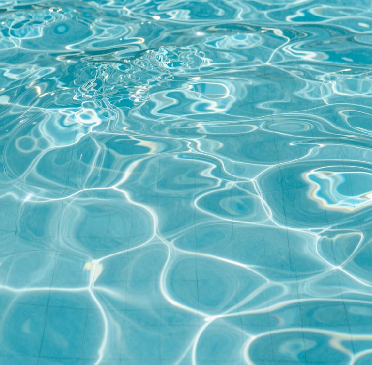 Macro shot of crystal-clear turquoise water rippling gently in a pool, clean geometric tile lines visible below, bright midday sunlight