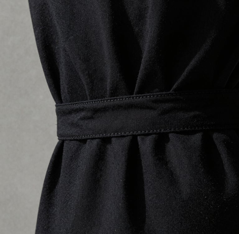 Stark minimalist fashion photography, extreme close-up of bound garment seams on heavy black cotton, high-contrast side-lighting emphasizing fabric weave texture, 35mm