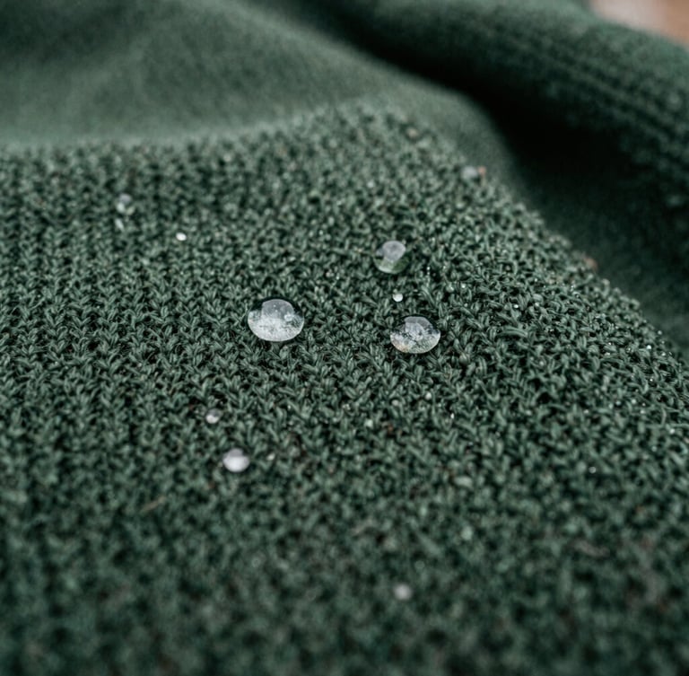 Macro close-up of water droplets beading on a dark green waterproof knitted blanket, overcast natural daylight, rich damp earth tones, sharp texture detail, 35mm