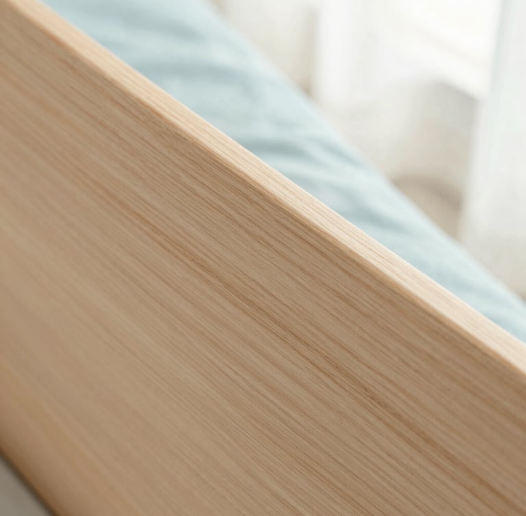 Tight macro shot of light ash wood grain, showing a smooth, polished surface, with a hint of pastel blue fabric in the background, soft diffused morning light.