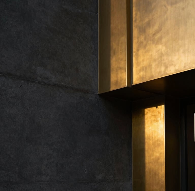 Tight straight-on geometric shot, dramatic high-end interior lighting, dark matte concrete wall meeting brushed brass architectural details.