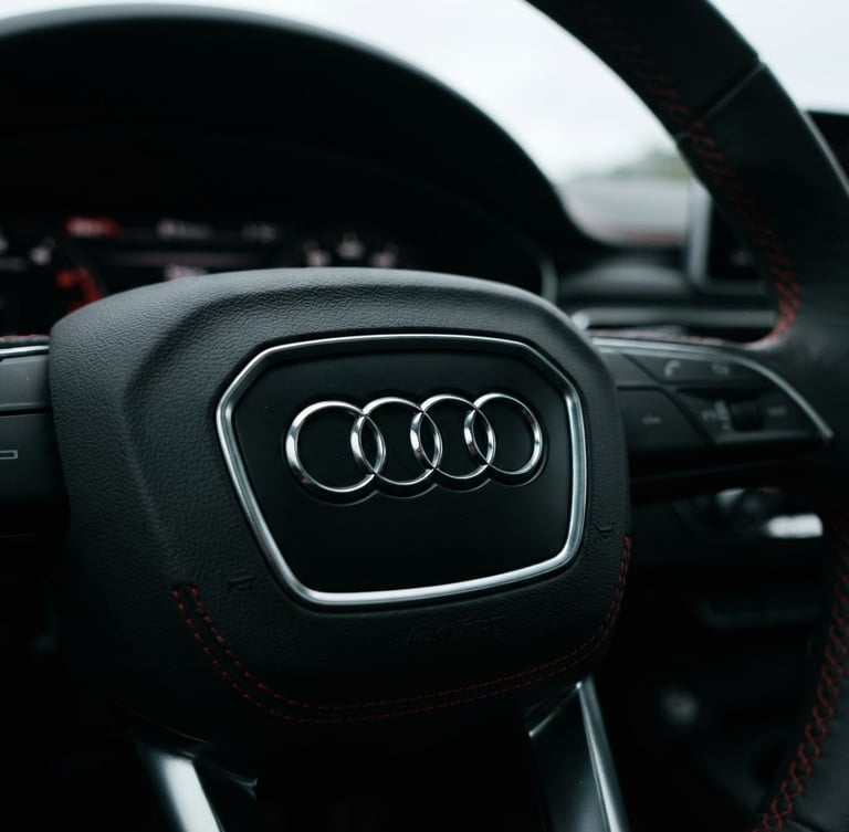 Low-angle close-up of a pristine metallic black Audi steering wheel badge, dramatic overcast daylight, sharp red dashboard stitching details, 35mm lens.