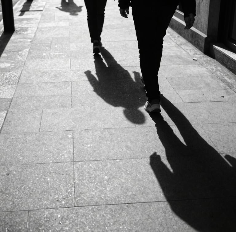 High-contrast street scene in London, harsh direct sunlight casting long deep shadows across concrete, a solitary figure walking, gritty 35mm tri-x film grain.