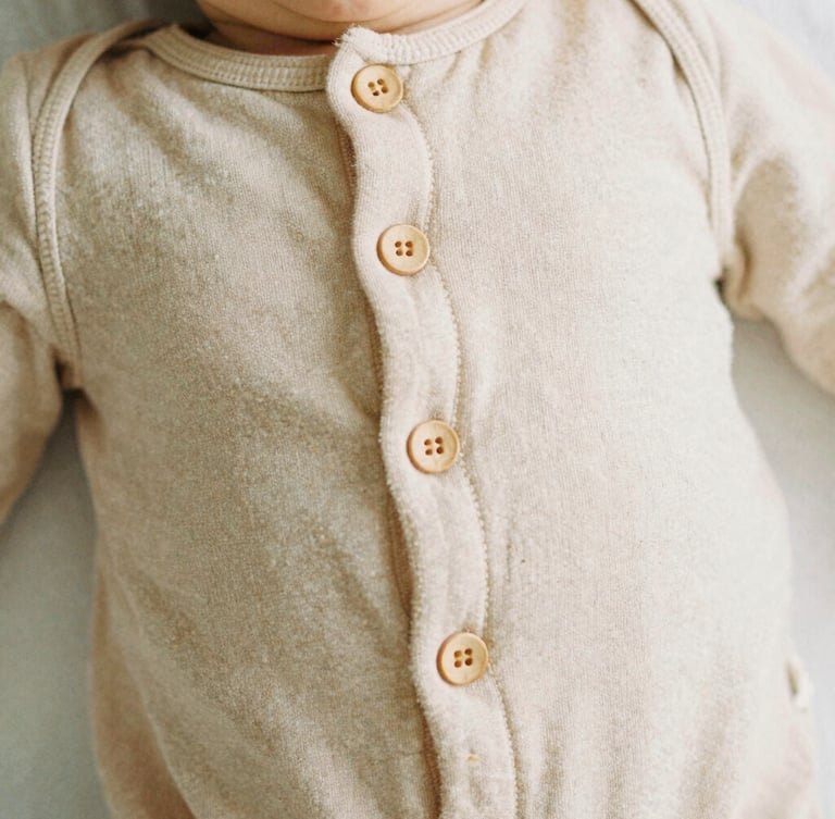 Close-up of soft organic cotton baby romper with delicate wooden buttons, warm beige textile texture, soft natural light, 35mm film look
