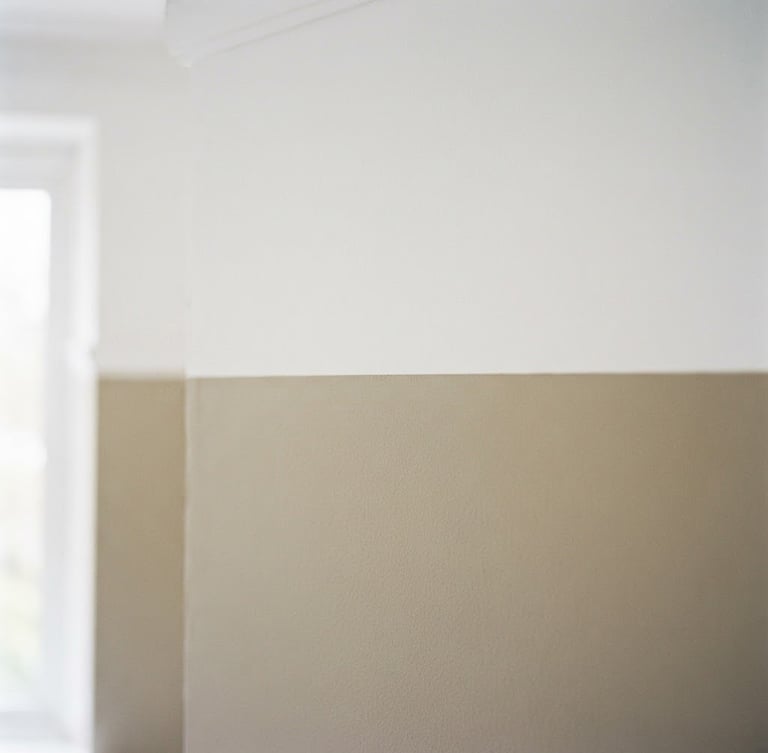 A sharp architectural crop of a perfectly taped, razor-sharp paint edge against a warm putty wall, soft natural window light, 35mm photography