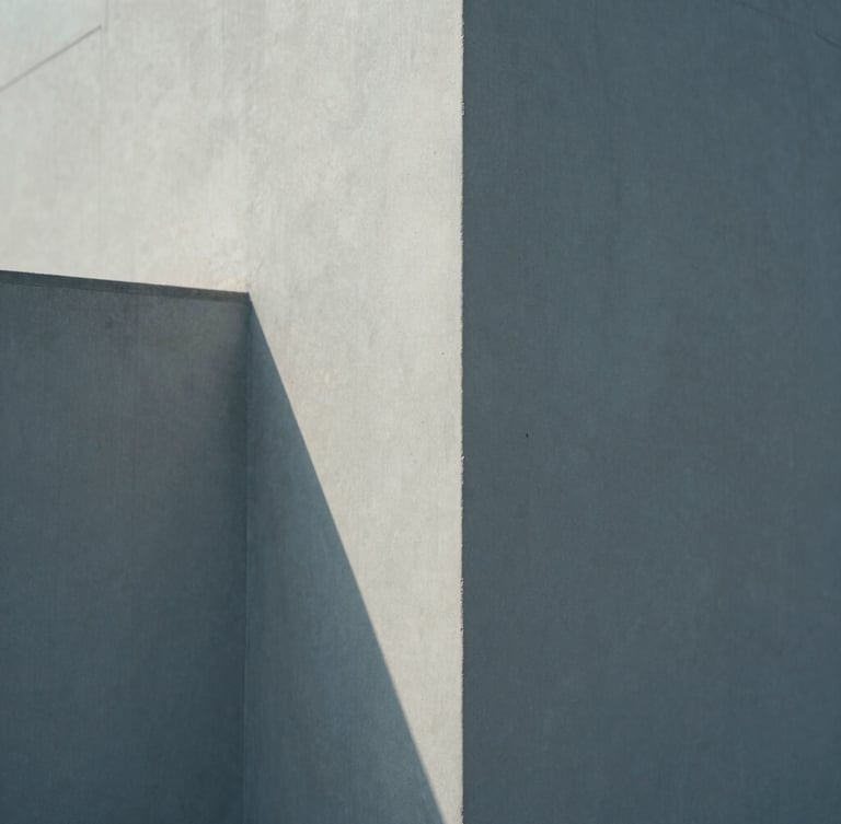 A minimalist, close-up photograph of architectural concrete angles casting clean geometric shadows under soft, diffused north-facing daylight.