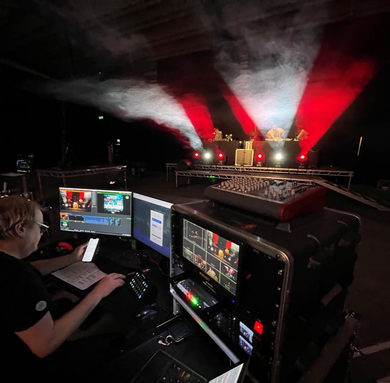 Video production technician managing a live stream event broadcast from a dark stage with red and white lighting.
