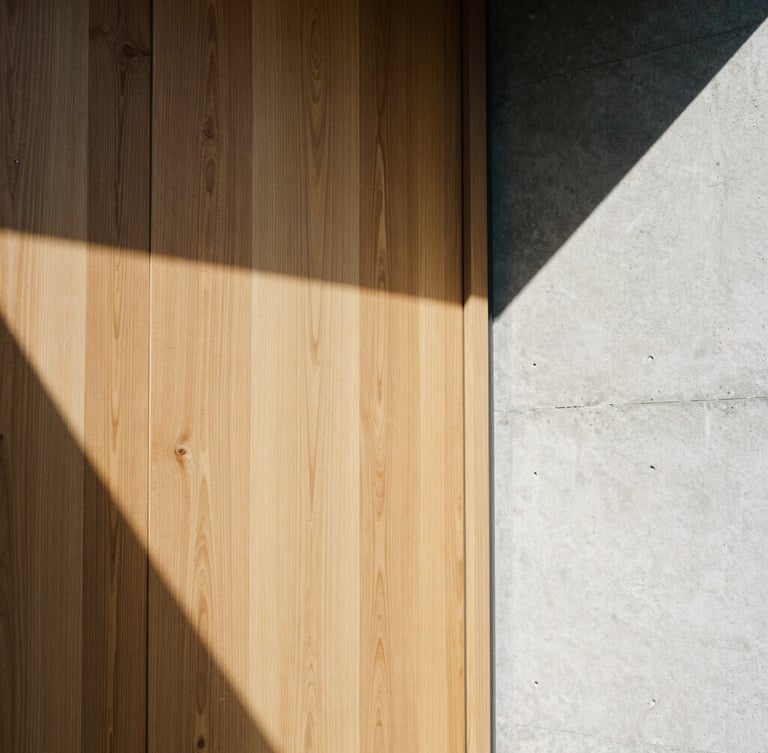 Portrait architectural film photography showing a tight detail crop of grain-matched oak panels meeting a polished concrete wall, sharp sunlight and high-contrast geometric shadows