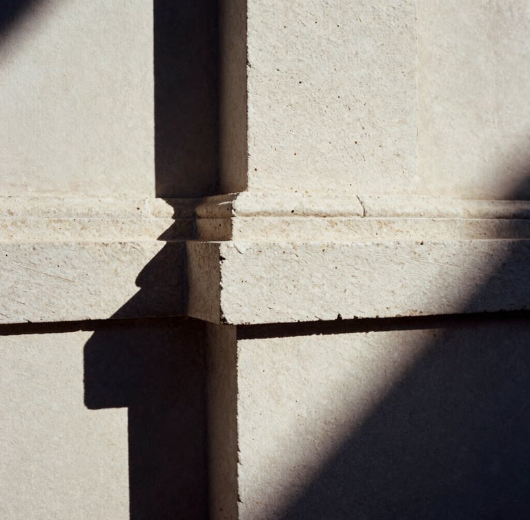 Close-up of hand-chiseled basalt stone junction meeting raw plaster, harsh high-contrast morning sunlight, deep shadows, 35mm film
