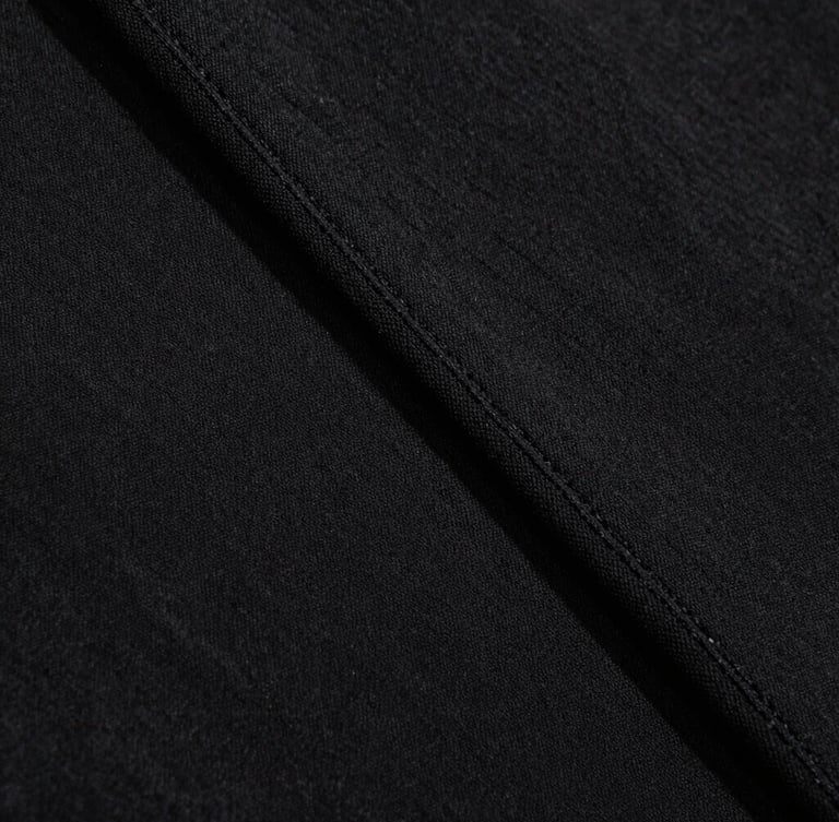Extreme close-up of heavy black cotton fabric texture, clean double-needle stitching, dramatic side lighting, 35mm film grain