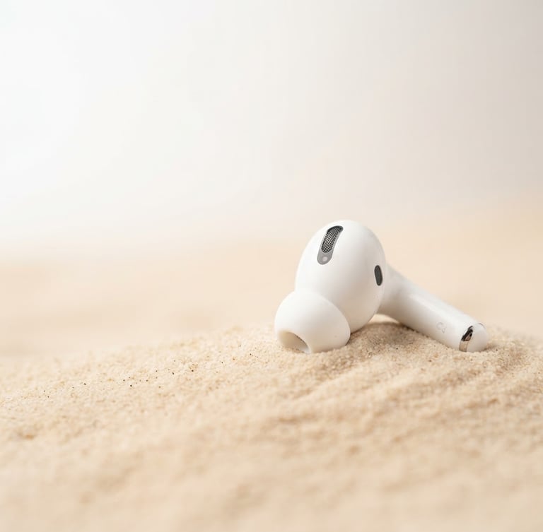 Premium wireless earbuds on a soft beige desert background, crisp studio light, 3/4 angle, ample negative space to the left