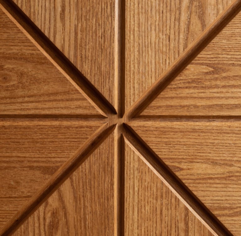 Macro side-lit shot of deeply routed geometric timber panel, sharp shadow-defining channels, amber-lit oak grain
