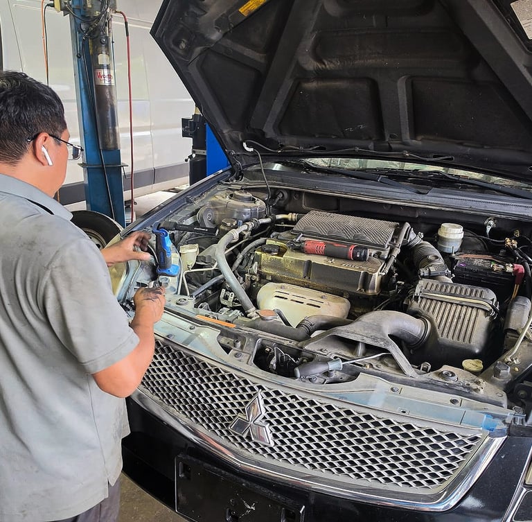 Professional auto mechanic inspecting a Mitsubishi car engine for repair at a garage.