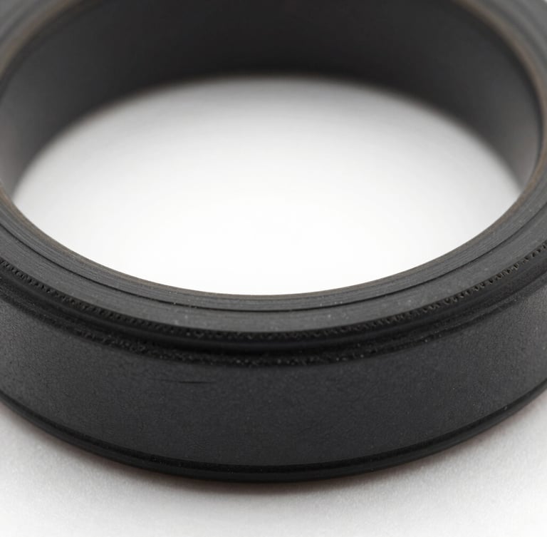 Macro studio photography of a custom-machined black elastomer O-ring showing dense material geometry and precise cross-section tolerances, high-contrast lighting.