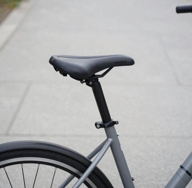 Close-up of a RealSeat comfort saddle mounted on a sleek grey commuter bicycle parked on a clean urban path, soft overcast daylight, desaturated tones, 50mm