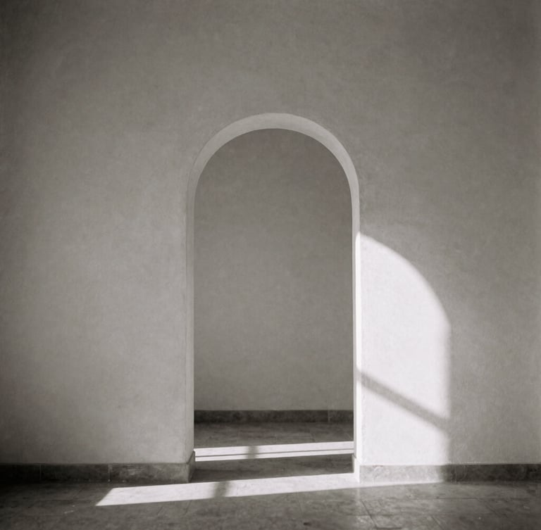 Minimalist black and white photograph with sepia undertones. A solitary stone archway casting a long, geometric shadow on an empty plaster wall, soft directional natural window light, elegant composition, 35mm film grain.