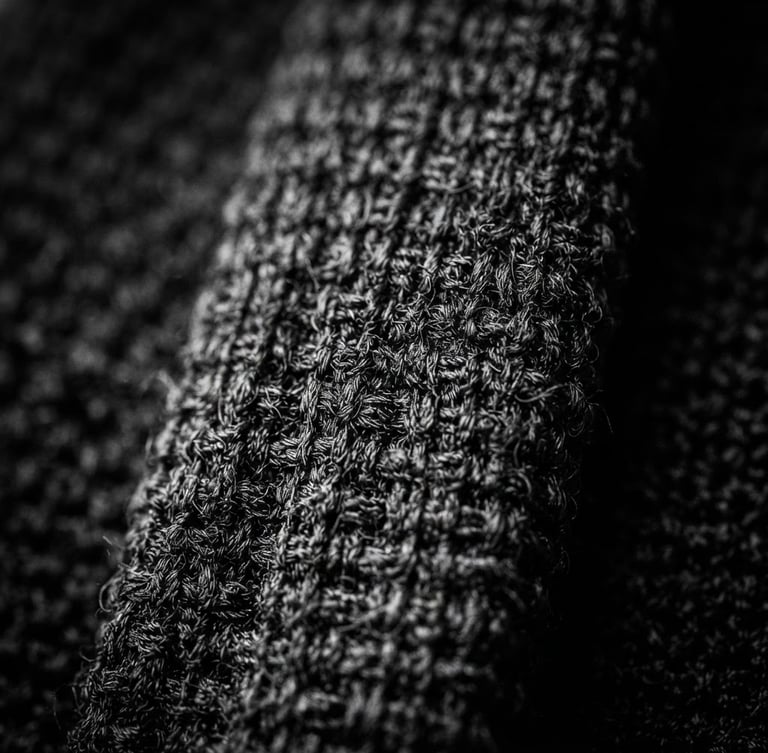 Extreme close-up of a textured black knitted silk tie, sharp focus on the knit grain, high-contrast monochrome photography, deep shadows, 85mm
