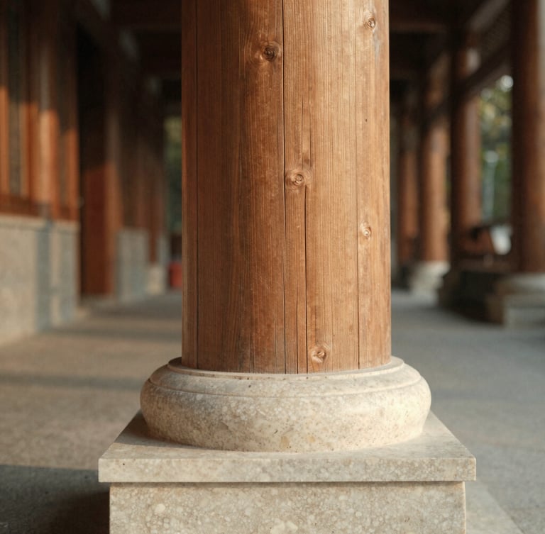 Close-up of a raw timber column meeting a hand-carved travertine base, soft diffused overcast daylight highlighting the coarse textures, deep perspective corridor behind, warm editorial photography.