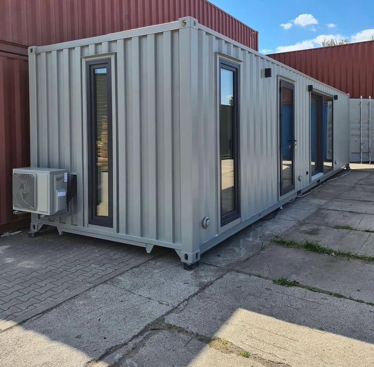 A gray shipping container home conversion with glass doors, windows, and an outdoor air conditioning unit.