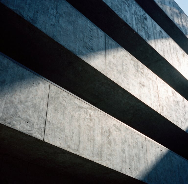 Architectural crop of a modern concrete building facade, sharp diagonal shadows, high-contrast side-lighting, 35mm film