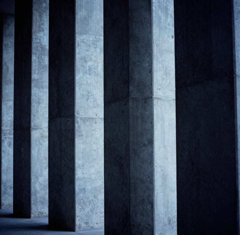 Architectural concrete lines with dramatic side-lighting, cool blue and deep charcoal tones, high-contrast shadows, 35mm lens.
