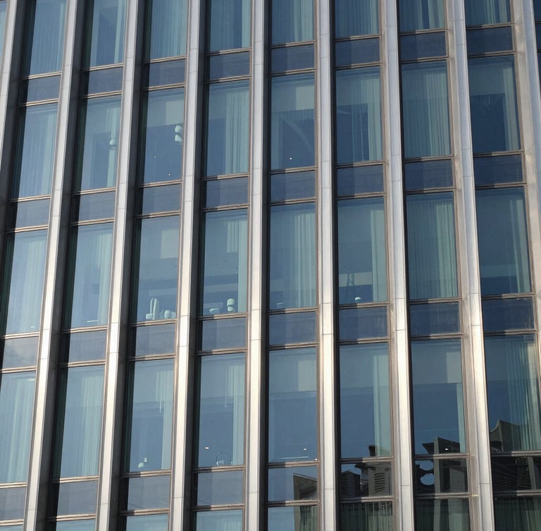 Close-up of structured glass and brushed steel facade of a modern corporate headquarters in Riyadh, sharp high-contrast daylight.