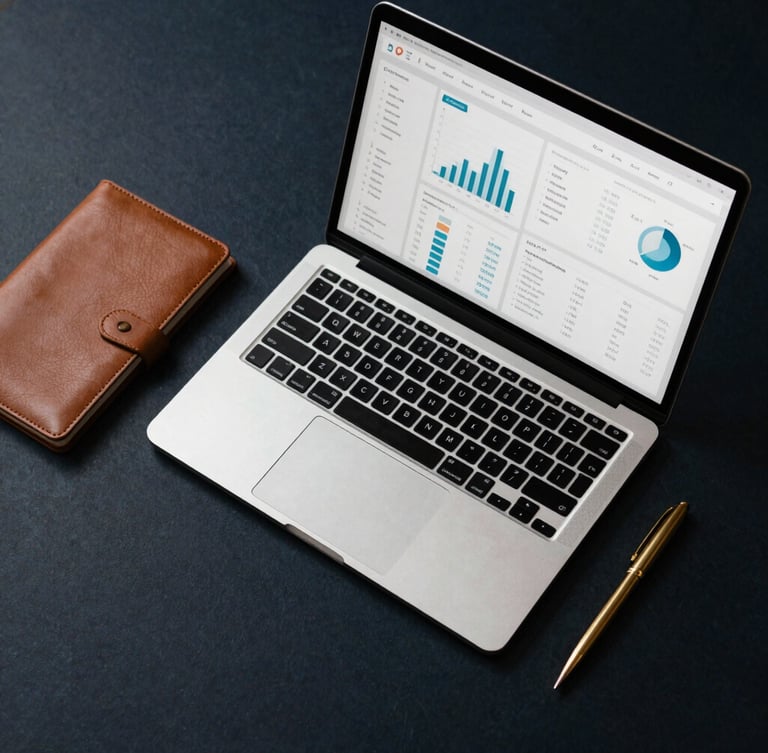 Overhead desk flatlay of a modern laptop showing clean analytics dashboards, a leather notebook, and a brass pen under dramatic directional light.