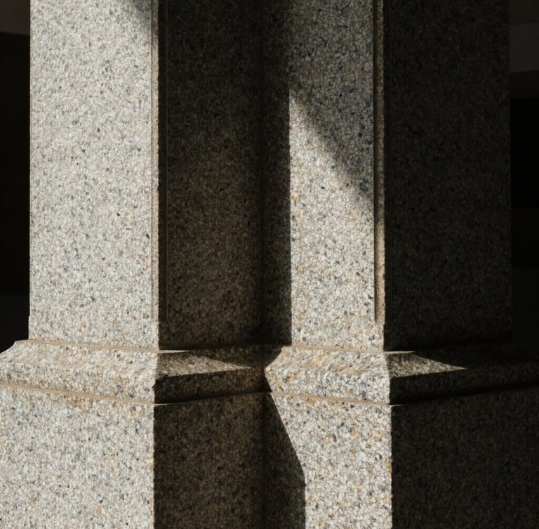 Macro close-up of a heavy, textured granite structural column, dramatic side-lighting casting deep shadows, architectural security.