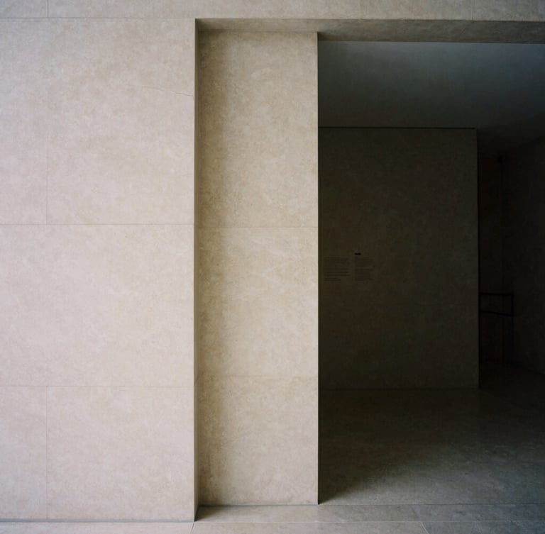 A minimalist architectural detail of a private gallery entrance, soft indirect natural light, deep quiet shadows, warm alabaster stone, medium format film