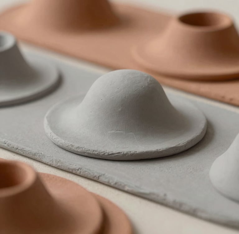 A close-up of layered clay models in soft ash gray and terracotta tones, casting subtle shadows under diffused natural studio light.