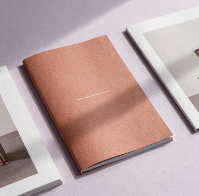 Staggered flat-lay of printed editorial lookbooks on a mist lavender background, soft natural daylight casting delicate shadows.