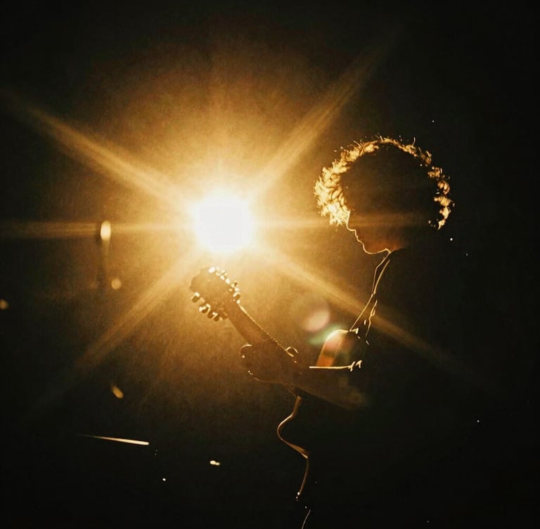 A dramatic backlit portrait of a musician holding a guitar, warm golden-hour light flares cutting through deep black negative space, high-contrast luminous editorial photography, 35mm
